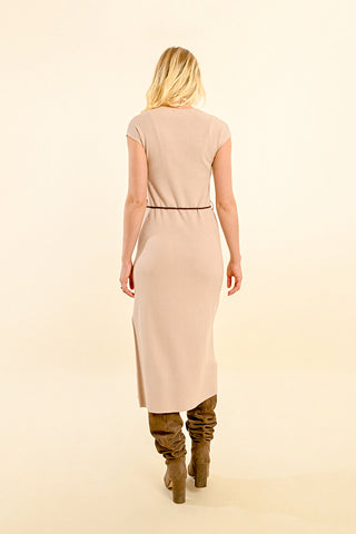 A woman with blonde hair wears the Molly Bracken Ribbed Knitted Midi Dress, featuring short sleeves and a self-tie belt, pairing it with tall brown boots as she stands facing away from the camera against a cream background.