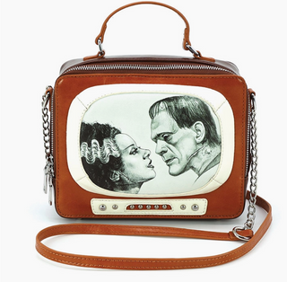 The Comeco Inc Glow in the Dark Frankenstein and Bride TV Bag features a top handle, chain strap, and showcases a vintage TV screen design with black-and-white art of Frankenstein’s monster and his bride facing each other.