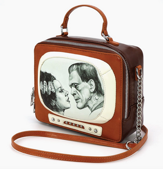 The Glow in the Dark Frankenstein and Bride TV Bag by Comeco Inc is a brown and cream retro TV-shaped handbag featuring Frankenstein’s monster and the Bride of Frankenstein facing each other on the front panel.