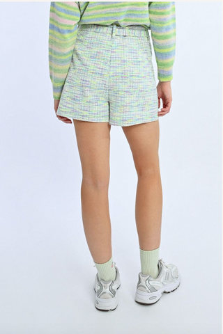 A person stands with their back to the camera, wearing Molly Bracken’s Knit Self-Tie Belt Shorts, a pastel striped sweater, light green socks, and white sneakers against a plain light background.