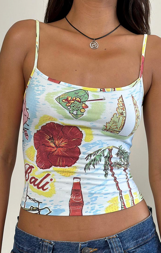 A woman wears the Motel Rocks Solay Bali Cami Top, featuring thin straps and vibrant tropical prints, paired with blue jeans and a black necklace.