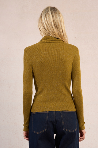 A woman with long blonde hair is seen from the back, wearing a Molly Bracken High Neck Knit Sweater in mustard yellow and dark blue jeans from the FW25 collection, set against a light beige background.