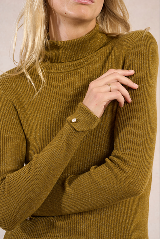 A person with long blonde hair touches their crossed arm, revealing a simple gold ring and a small button at the cuff of a Molly Bracken High Neck Knit Sweater in ribbed mustard yellow.
