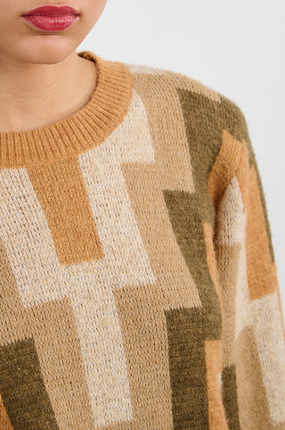 A close-up shows the lower face, neck, and upper chest of a person wearing the Molly Bracken Retro 80s Knit Sweater, featuring soft acrylic poly wool in beige, tan, cream, and olive green geometric patterns.