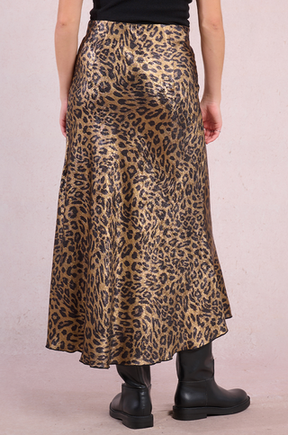 A person wears the Molly Bracken Gold Metallic Leopard Midi Skirt with black boots, shown from the back against a light pink background.