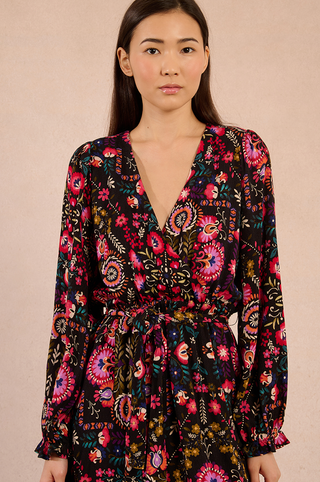Irina wears the Molly Bracken Irina Print Maxi Dress, a black multico viscose piece adorned with red, pink, and yellow florals. With long sleeves, a V-neck, and tied waist, it stands out beautifully on any neutral background.
