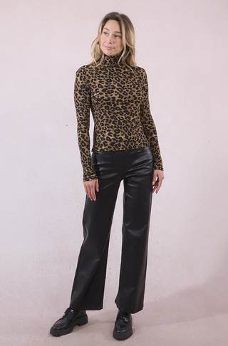 A woman with shoulder-length blonde hair smiles softly as she poses against a light pink background, wearing the Molly Bracken High Neck Leopard Top, black faux leather wide-leg pants, and black shoes.