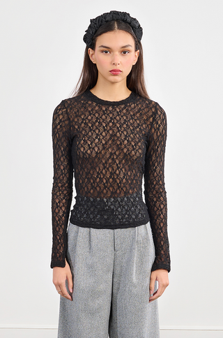 A woman stands facing forward in a Molly Bracken Lace Stretch Top, gray high-waisted trousers, a black headband, and a sleek black smartwatch against a white background. Part of the Rename FW25 collection.