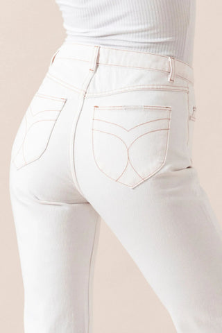 A person shown from the waist down, viewed from the back, wears Rollas’ Classic Straight Ankle Denim in 80s White with light brown stitching and distinct pockets, paired with a ribbed white top.
