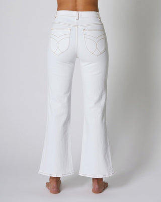 A person stands barefoot, facing away from the camera, wearing Rollas Classic Straight Ankle Denim in 80s White against a plain light background.