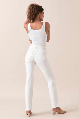A woman stands facing away, wearing Rollas Classic Straight Ankle Denim in 80s White with a white ribbed tank top and beige heeled shoes. Her hair is tied back as she poses against a neutral background.