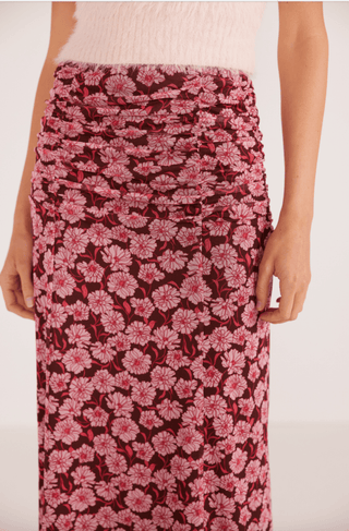 A person wears a fluffy white top and the MINKPINK Dakota Mesh Midi Skirt-FINAL SALE, with a ruched waist and pink/red floral pattern. The cropped photo shows them from shoulders to knees.