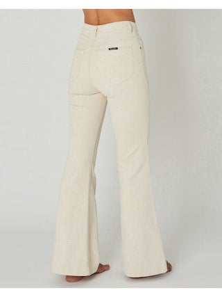 A person stands barefoot, facing away in Rollas East Coast Flare Corduroy-FINAL SALE high-waisted cream jeans with back pockets and seam details, capturing a relaxed coastal vibe against a plain background.