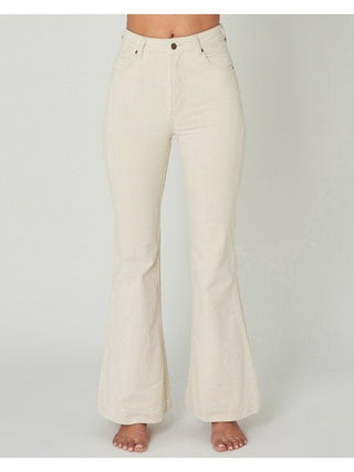 A person stands barefoot against a plain background, wearing the Rollas East Coast Flare Corduroy-FINAL SALE jeans in cream, high-waisted with front pockets and button closure. The cropped frame evokes an effortless coastal living style.