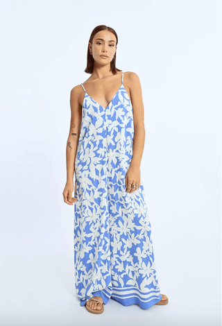 A woman in the Molly Bracken Floral Strappy Jumpsuit-FINAL SALE, featuring thin straps, pairs it with sandals and stands against a plain light background.