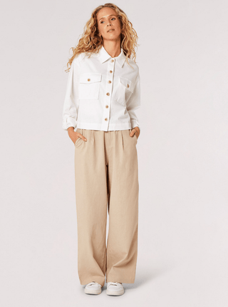 A woman stands with hands in the pockets of her wide-leg beige pants, wearing the Apricot Lightweight Crop Jacket-FINAL SALE and white sneakers, set against a plain light background.