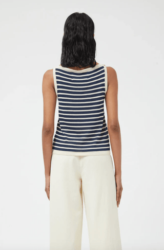 A person with shoulder-length dark hair is seen from behind, wearing the Compania Fantastica Nautical Stripe Knit Tank Top-FINAL SALE and cream pants against a plain light background.