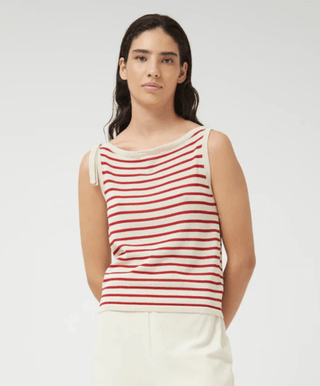 A woman with long dark hair stands against a plain background, wearing the Compania Fantastica Nautical Stripe Knit Tank Top-FINAL SALE. The sleeveless top features red stripes, a boat neckline, and a tie detail on one shoulder.