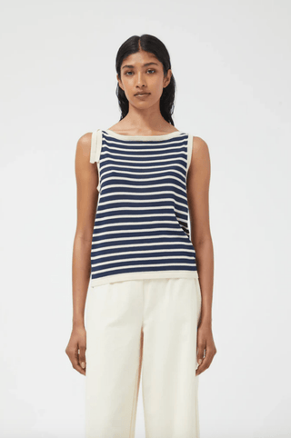 A woman faces forward in a Compania Fantastica Nautical Stripe Knit Tank Top-FINAL SALE, featuring a boat neckline and tie shoulder, paired with loose cream pants against a plain light background.