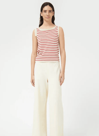 A woman faces forward, wearing a sleeveless Compania Fantastica Nautical Stripe Knit Tank Top-FINAL SALE with red stripes and high-waisted, wide-leg cream pants against a plain white background.