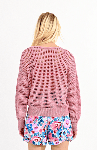 A woman with long blonde hair is shown from the back wearing the Molly Bracken Open Weave V-neck Knit Sweater-FINAL SALE in pink and colorful floral shorts against a plain white background.