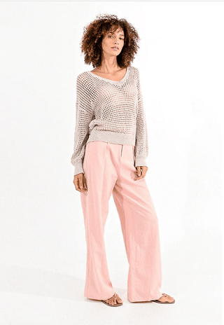 A woman with curly hair models the Molly Bracken Open Weave V-neck Knit Sweater-FINAL SALE in beige, paired with light pink wide-leg pants and sandals, standing against a plain white background.