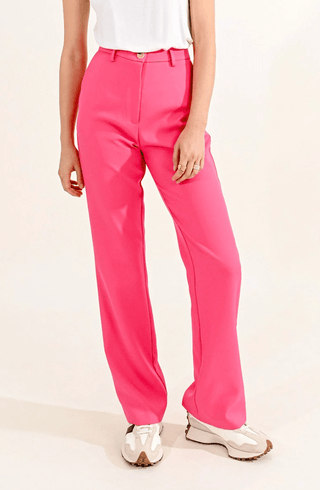 A person, visible only from the waist down, stands against a plain light background wearing bright pink Priscilla Pants-FINAL SALE by Molly Bracken, paired with a white sleeveless top and white sneakers.