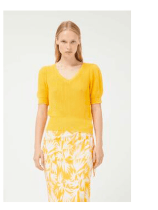 A woman with straight, light blonde hair wears the Compania Fantastica Short Sleeve Knit Sweater-FINAL SALE in bright yellow and a white skirt with a bold yellow floral pattern, standing against a plain light background.