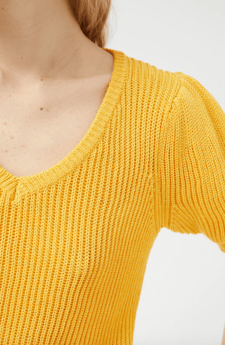 A person wears the Compania Fantastica Short Sleeve Knit Sweater-FINAL SALE, featuring a textured, bright yellow V-neck design. Only the upper torso, shoulder, arm, and neck are visible against a plain background.
