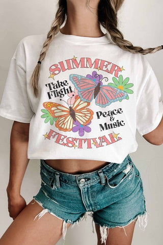 A woman wears the WKNDER Summer Festival Cropped Unisex Graphic Tee—FINAL SALE, featuring colorful butterflies and festival-inspired text, styled with high-waisted denim shorts.