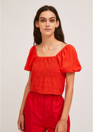 A woman with long dark hair wears the Compania Fantastica Smocking Crop Top With Puff Sleeves-STREET SALE in bright red, paired with matching high-waisted red pants, standing against a plain light background.