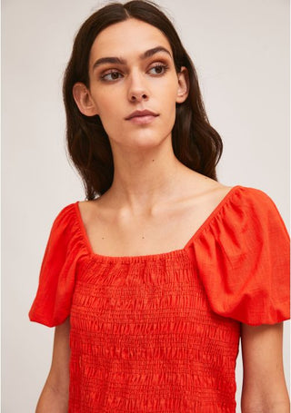 A woman with long dark hair wears the Compania Fantastica Smocking Crop Top With Puff Sleeves-STREET SALE, a bright red, square-neck top with a smocked bodice and short puff sleeves, against a plain light background.