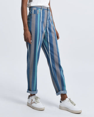 A person wears Molly Brackens Stripe Denim Pants-FINAL SALE, featuring cuffed, high-waisted vertical blue and gray stripes, paired with a white top and sneakers, standing against a plain light background.